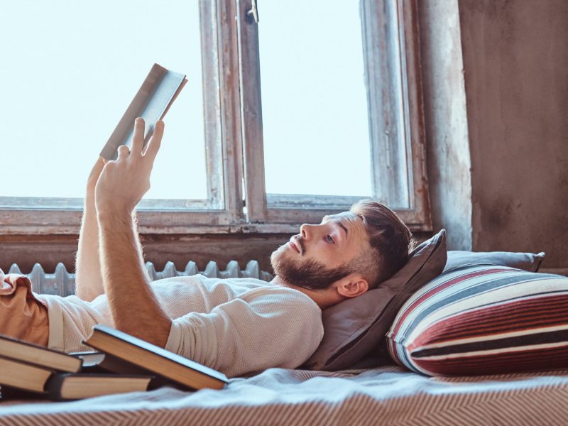 Portrait of a handsome student guy reading a book in his bed.